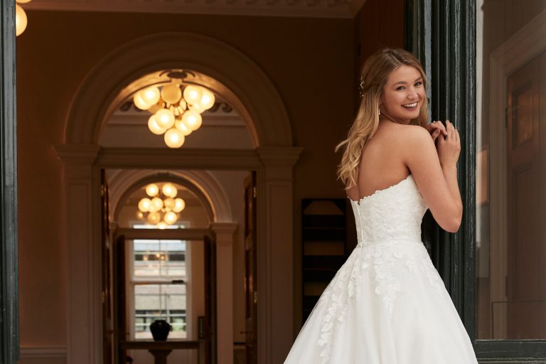 A beautiful young bride at the entrance to Winslade Manor. The bride is dressed in a full length wedding dress and is smiling as she looks over her right shoulder