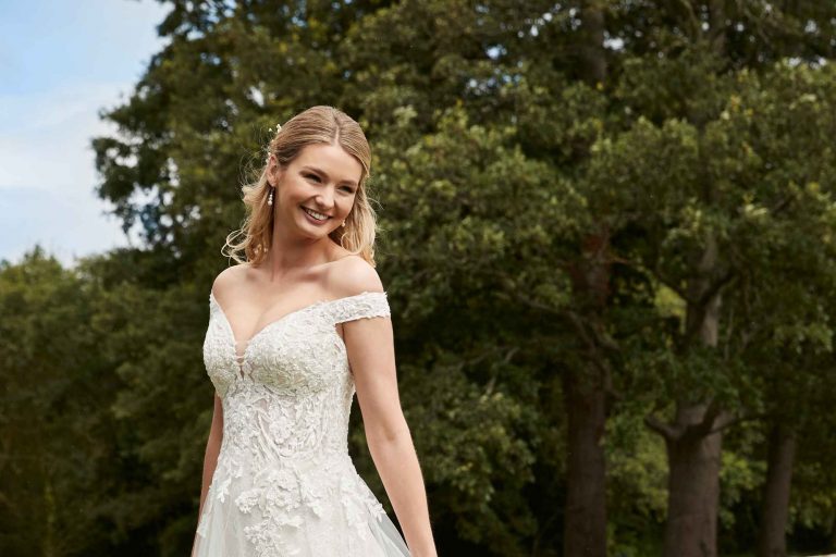 A smiling bride on the lawn at Winslade Manor. She is holding the sides of her elaborate embroidered wedding dress as she smiles, happily contemplating the day ahead