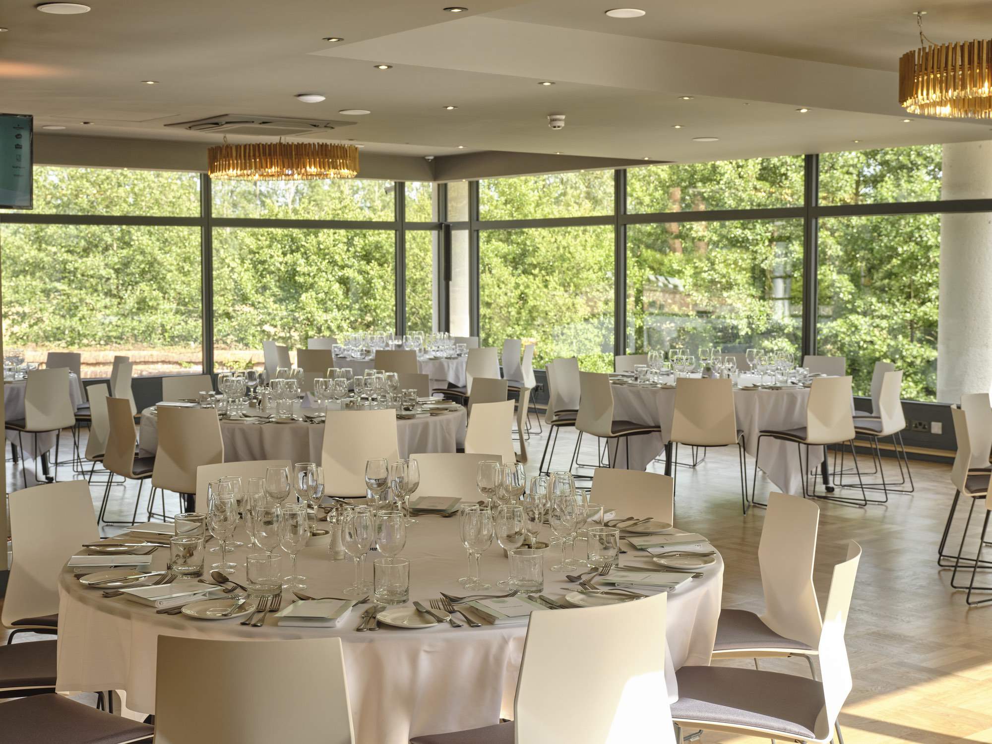 Large event space with full height glazing and round tables set with white linen table settings for an event at The Forge