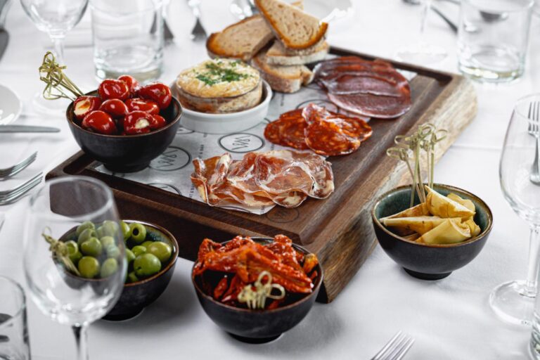 A charcuterie board with stuffed peppers, humous and bread. The board is on a white linen table set for a wedding meal in The Forge