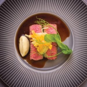 A dark place with two slices of beef fillet and seasonal vegetables surrounded by a rich sauce